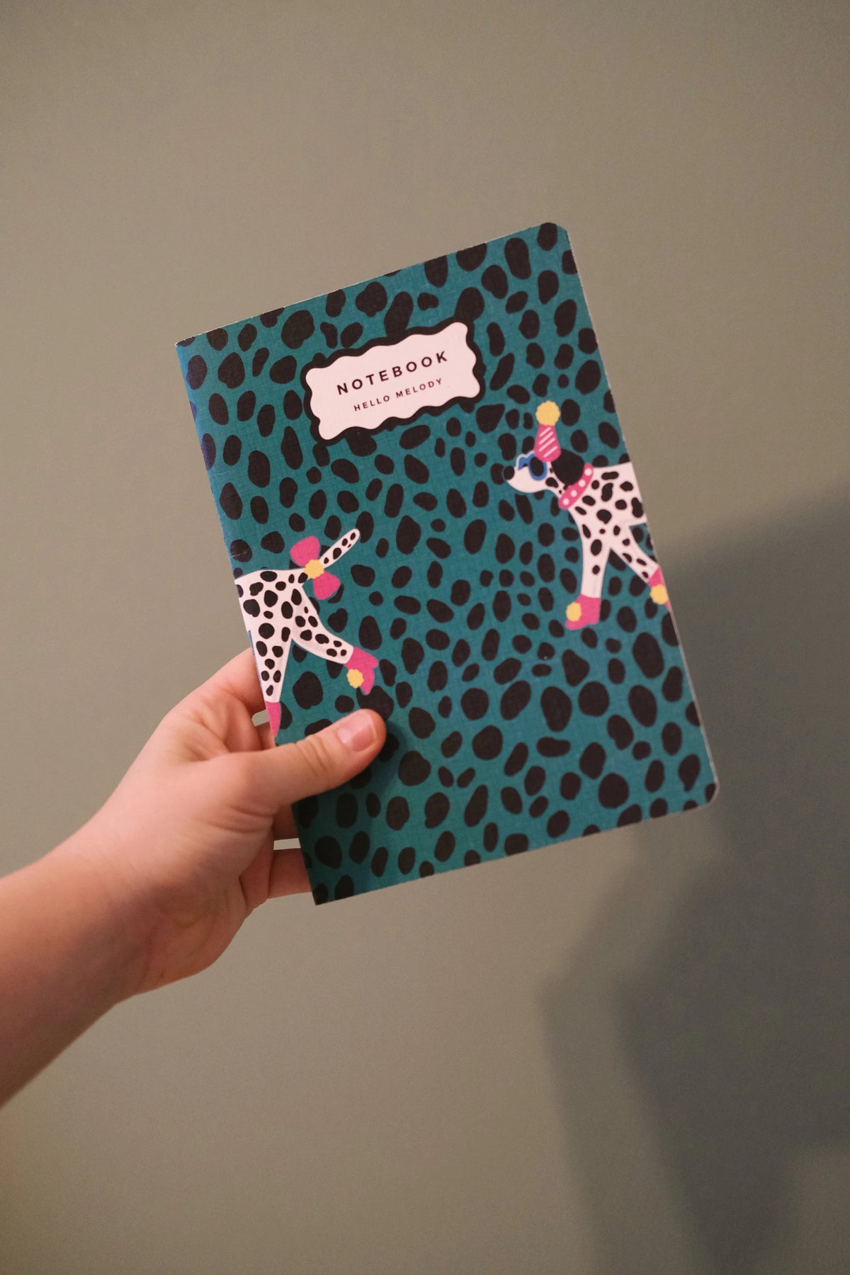 Dalmatian notebook held upright, showing its green spotted cover and illustrated dogs.