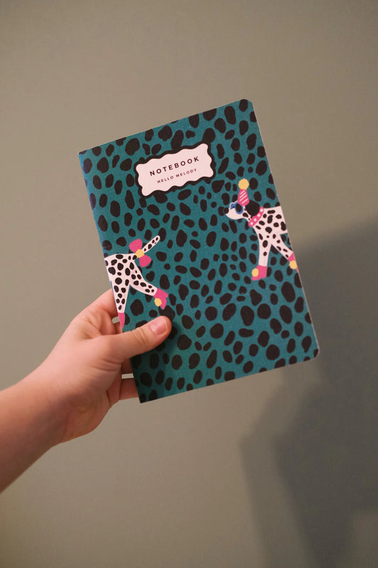 Dalmatian notebook held upright, showing its green spotted cover and illustrated dogs.