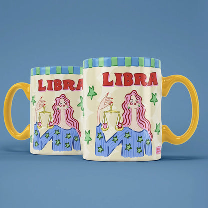 Two Libra star sign mugs showing a pink-haired figure holding golden balance scales